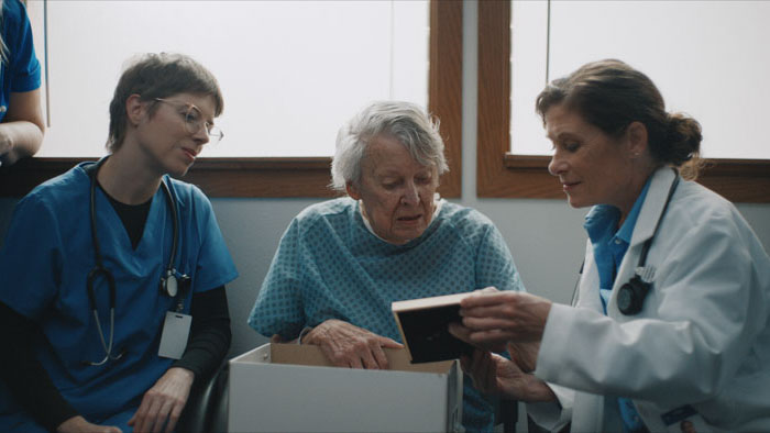 Peggy Trojan as Gladys examines a box with Dr. Vobernik and a nurse in Winter Hymns.