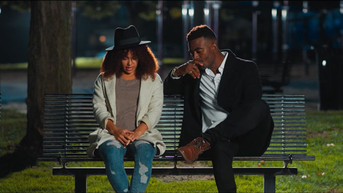 Imani and Ike sit on a park bench at night in Yellow Broken Road, a tense silence between them.