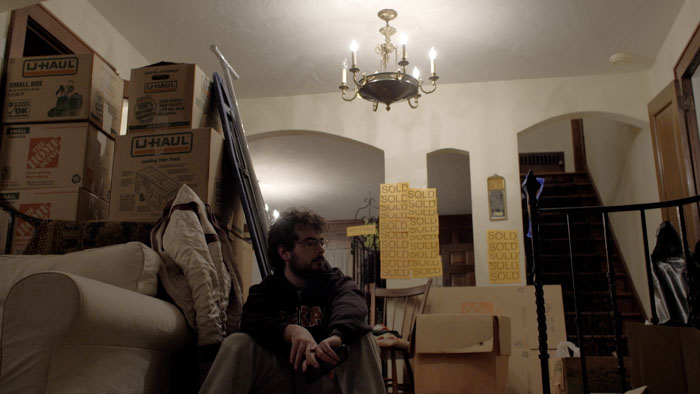 Andrew Garbus sits among moving boxes and SOLD signs in Everything I Own.