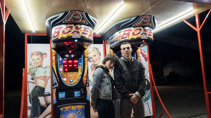 Gigi (Francesco Gheghi) and Giulia (Tecla Insolia) stand together at a carnival arcade in Familia.