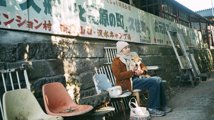 Yuta (Tasuku Emoto) holds a dog outside a rural building in Memorizu.