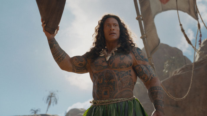 Maui (Dwayne Johnson) raises a paddle aboard his canoe in Disney's live-action Moana.