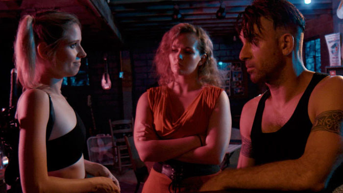 Cecilia (Nicole Mattox) talks with two companions in a dim bar in Red Days 2: Cecilia.