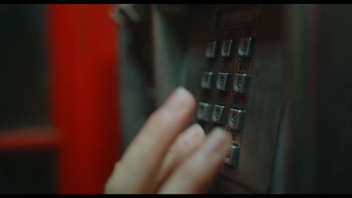 Stephanie (Sarah Lambie) dials a payphone at midnight in Satoru.