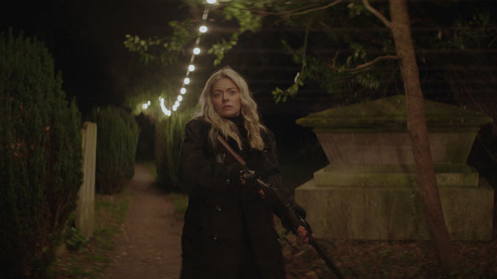 Nemesis Knight (Nicole Bartlett) carrying a rifle through a dark cemetery in The Phantom Warrior.
