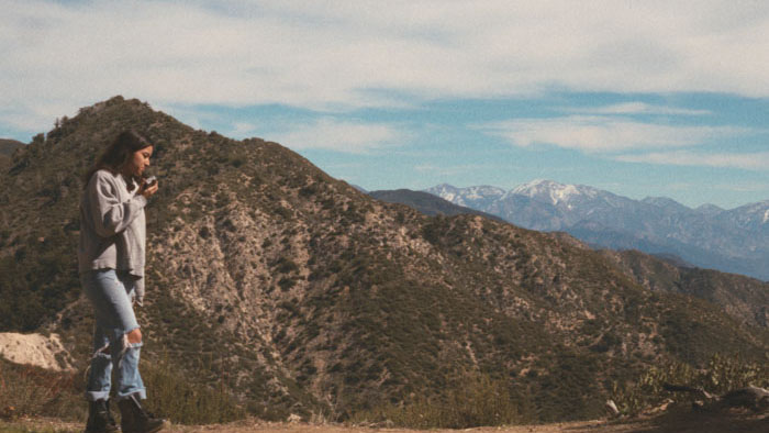 Skai (Jasmine Lee Brim) listens to Amy's cassette tape on a mountain trail in Torn Together.