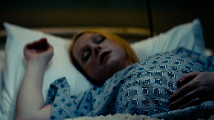Alice Booker (Llana Barron) lies in bed as a hand reaches toward her in Angels Near Death.