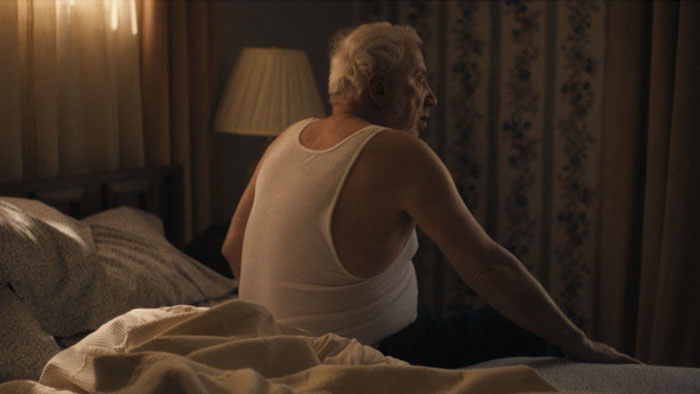 Sasha (Elya Baskin) sits at the edge of his bed in a quiet morning scene from Dance With Me.