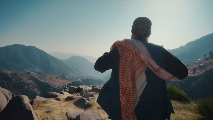 A man in traditional dress looks out over the mountains in Hanging by a Wire.