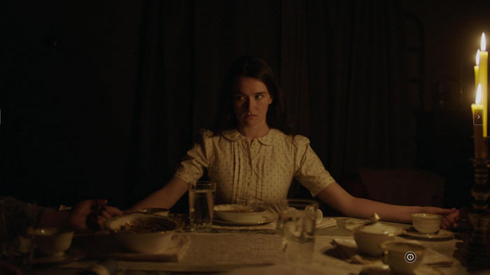 Maeve (Sarah Pidgeon) sits tensely at a candlelit dinner table in Lazareth.
