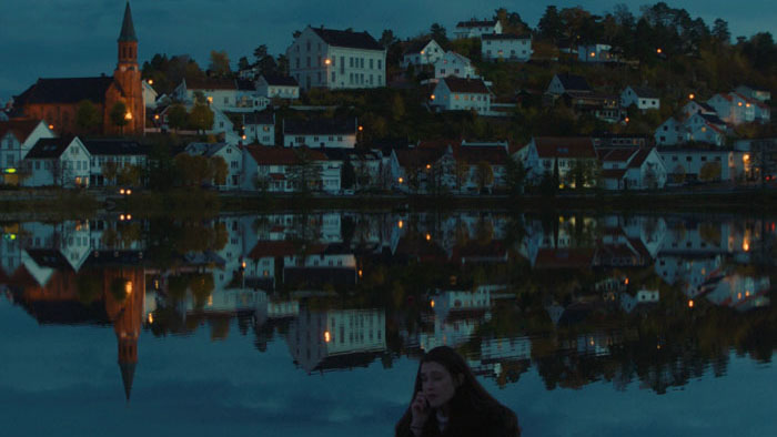 Evelyn (Heather Cunningham) sits by the water at night in a Norwegian town in Life At Sandy's.