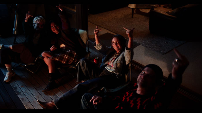 Friends gather on a porch at night in Our Effed Up World, pointing skyward.