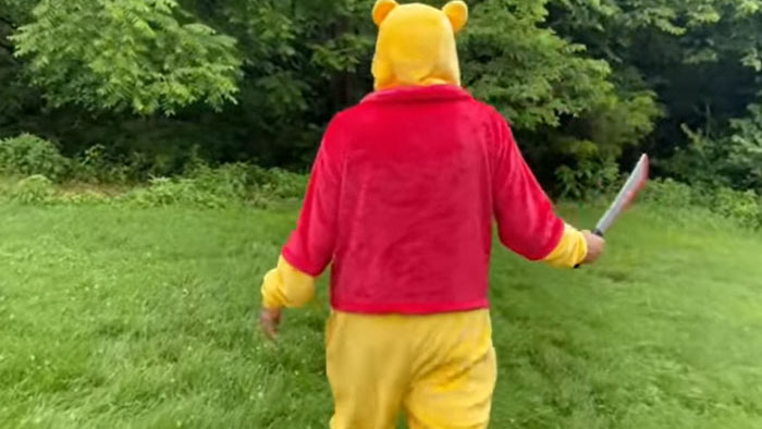 A Pooh costume figure grips a knife walking through grass in Pooh Goes to the Woods: The Final Adventure.