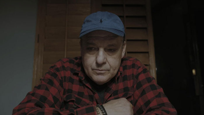 Tom Sizemore as Hank sits indoors in a tense video interview in Project Skyquake.