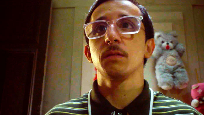 Tomas (Rodrigo Noya) sits in his cluttered room surrounded by dolls in The Dollmaker.