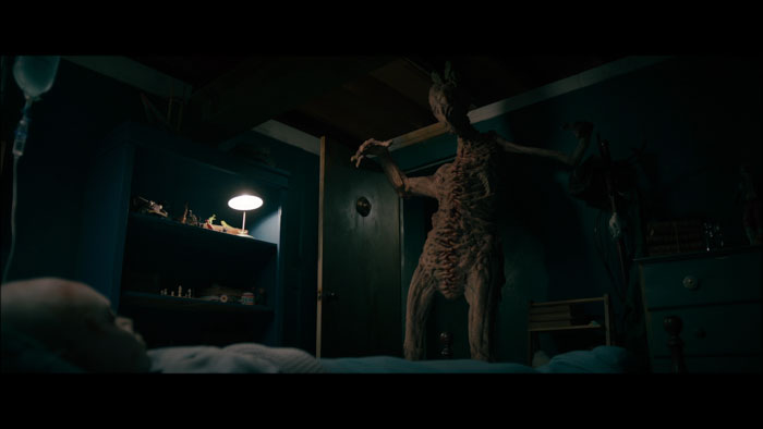 A grotesque supernatural entity looms in a bedroom doorway in The Room Below.