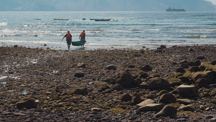 Two fishermen carry their catch ashore on a rocky beach in the documentary Arubara.