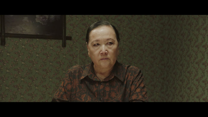 Farida (Kalicha Seidaliev) sits coldly in a floral-wallpapered room in Burning.