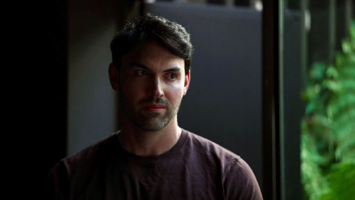 Oliver (Arron Blake) looks troubled in a dim apartment in Cuddle.