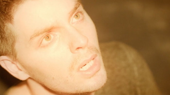 A man is seen in extreme close-up under warm light in a scene from Isolation.