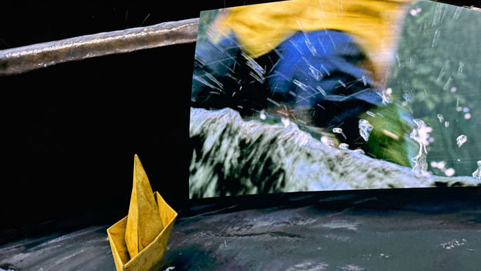 A yellow paper boat sails beneath Georgie's rain-soaked screen at the IT in Shared Reality premiere at Cosm.