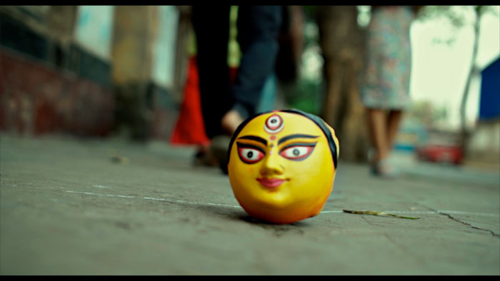 A painted Durga idol face rests on a cracked sidewalk in LegXpression.