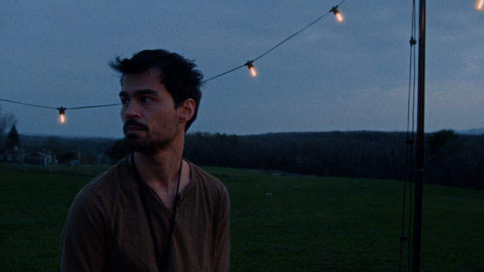 Jerome (JJ Bozeman) stands beneath string lights at dusk in Loving Silence.