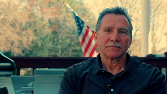 Brad Hores, FDNY firefighter, sits for an interview with an American flag behind him in Memories From Ground Zero.